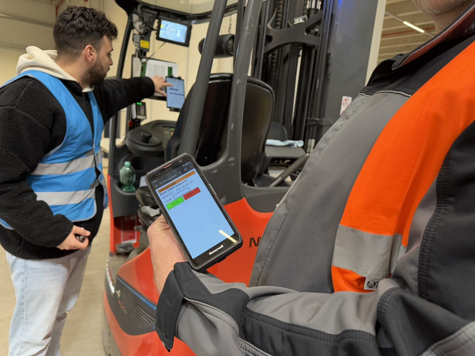 Mitarbeiter am mobilen Terminal des Flurförderzeugs, ein Kollege steht daneben.