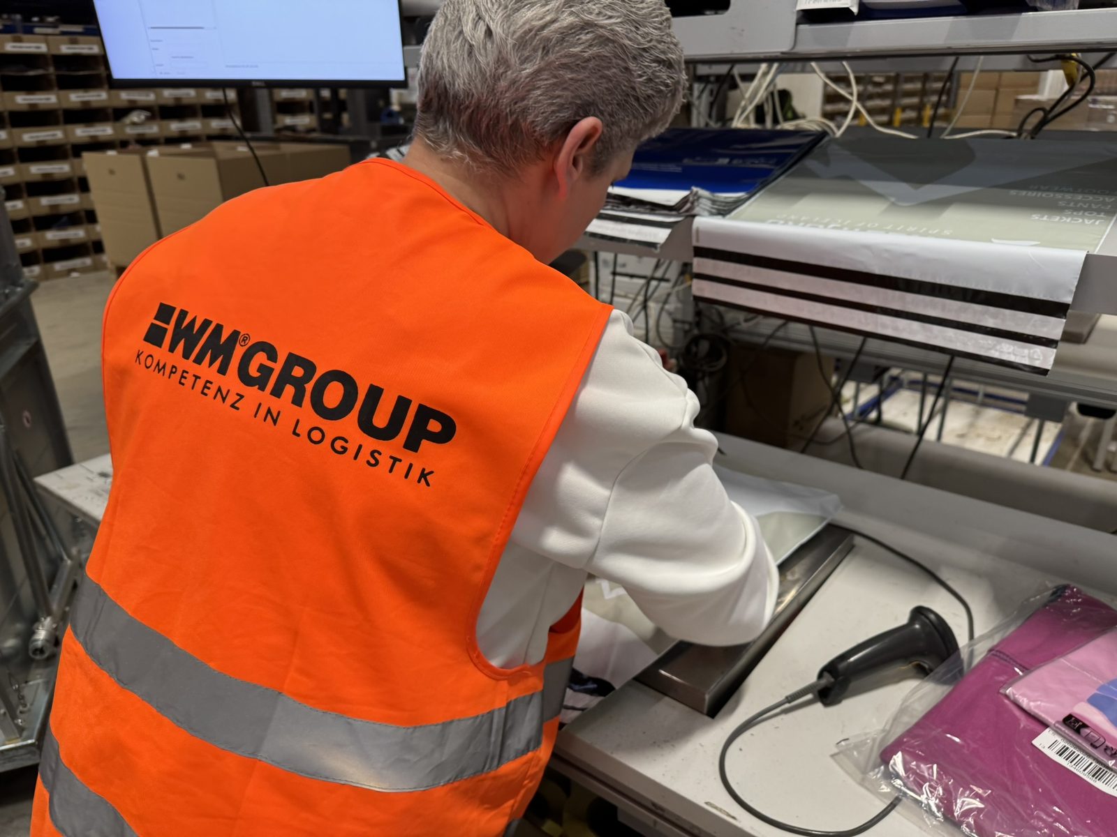 Mitarbeiterin in WM-GROUP-Warnweste verschließt eine Sendung an der Verpackungsmaschine.